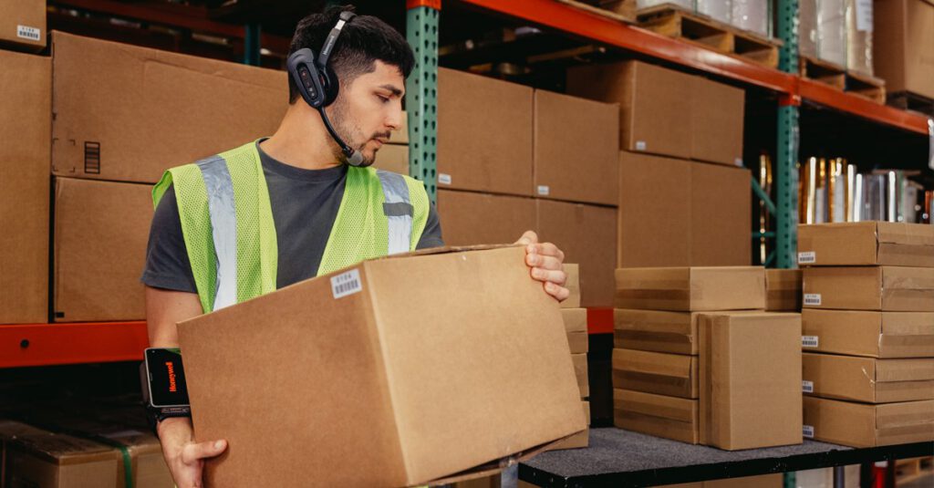 A warehouse worker transporting a package while wearing a voice-directed headset