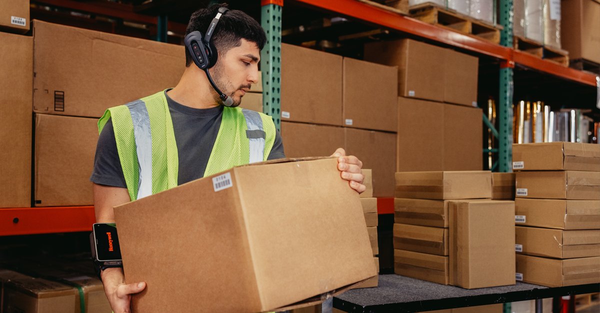 A warehouse worker transporting a package while wearing a voice-directed headset