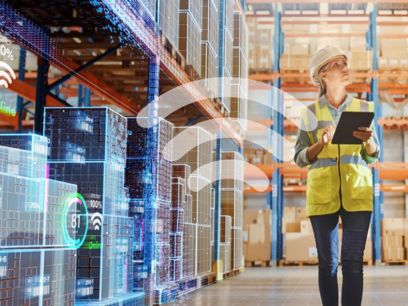 A woman in a warehouse with a tablet and wireless icon overlayed.