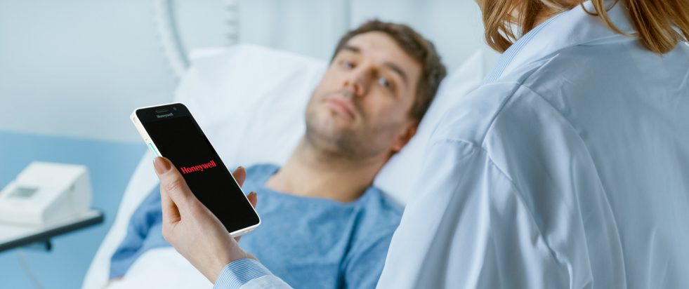 A healthcare worker using a smartphone with the word Honeywell on the screen