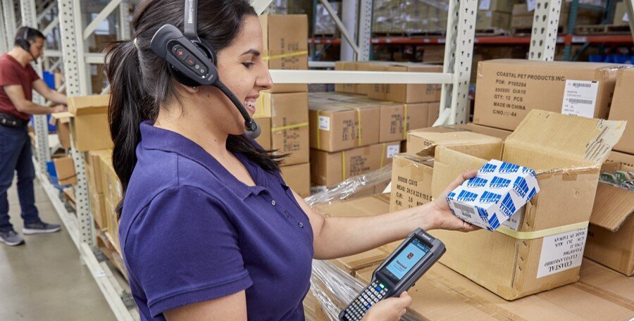 A woman wearing a voice-directed headset with a handheld barcode scanner
