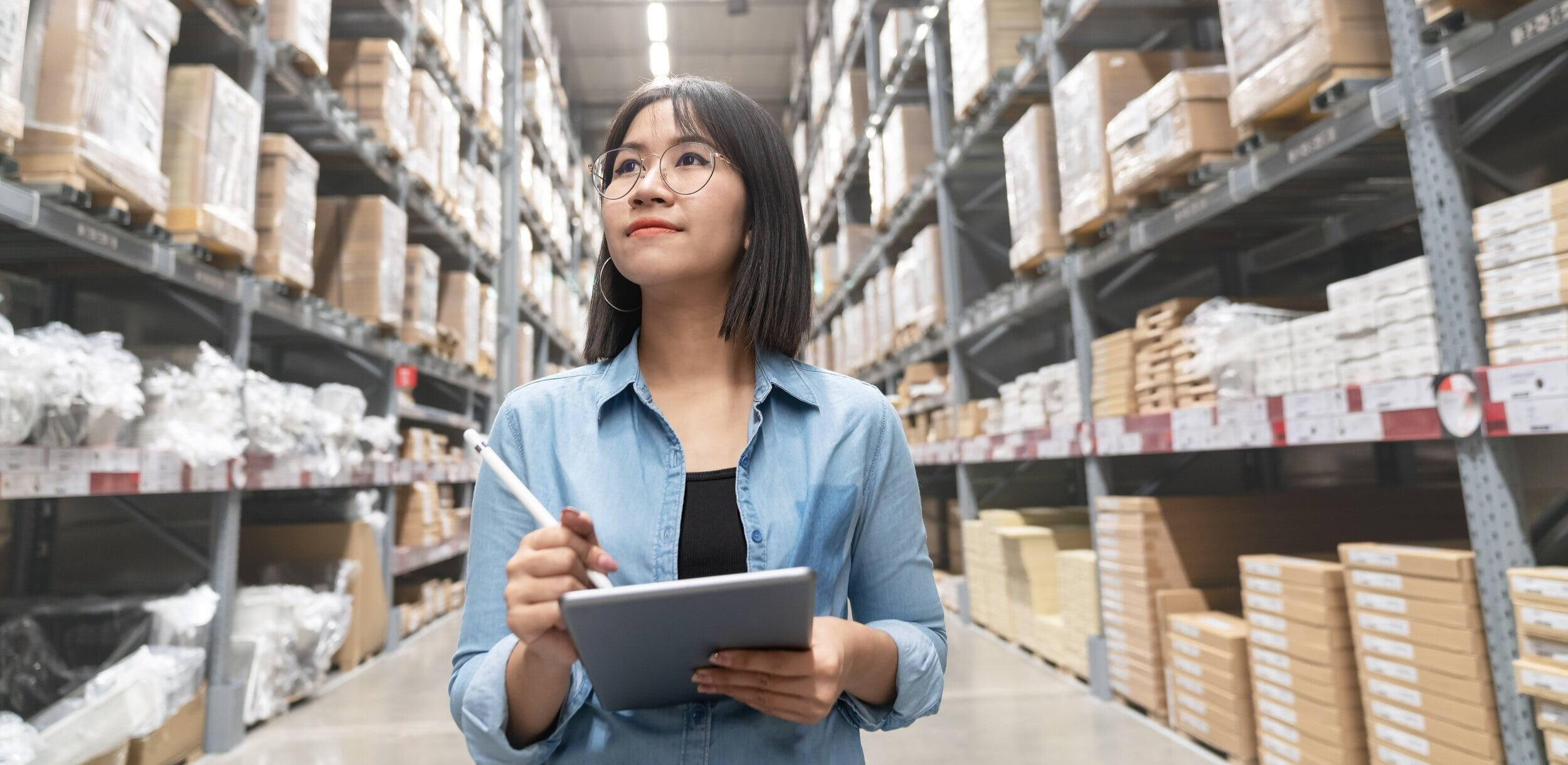 A woman using a tablet and stylus in a warehouse