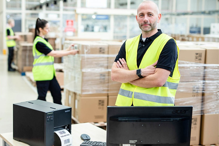 A worker standing by a barcode printer in a warehouse
