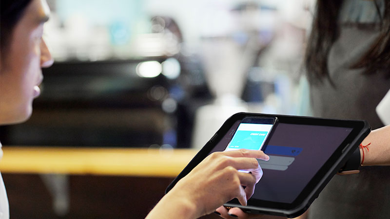 A woman using a smartphone to make a payment on a tablet