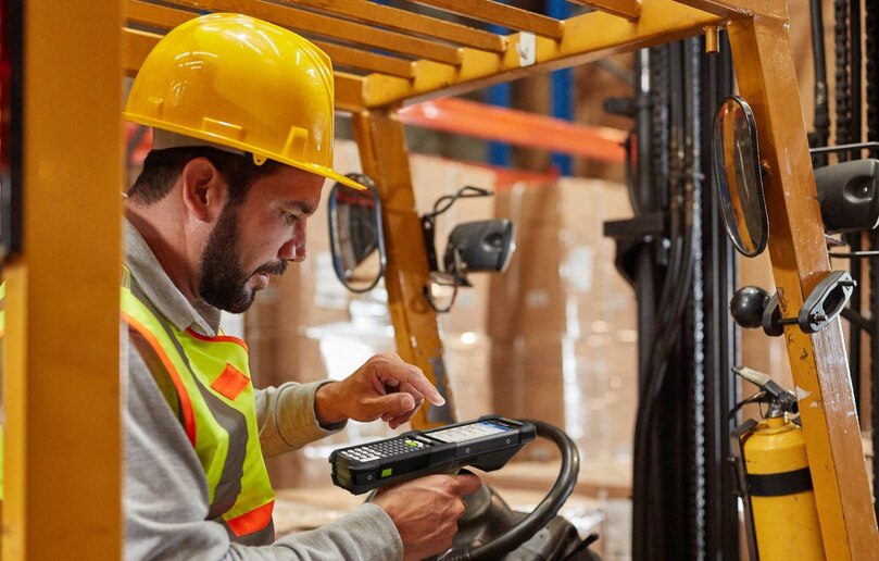 A man on a warehouse forklift using a mobile device